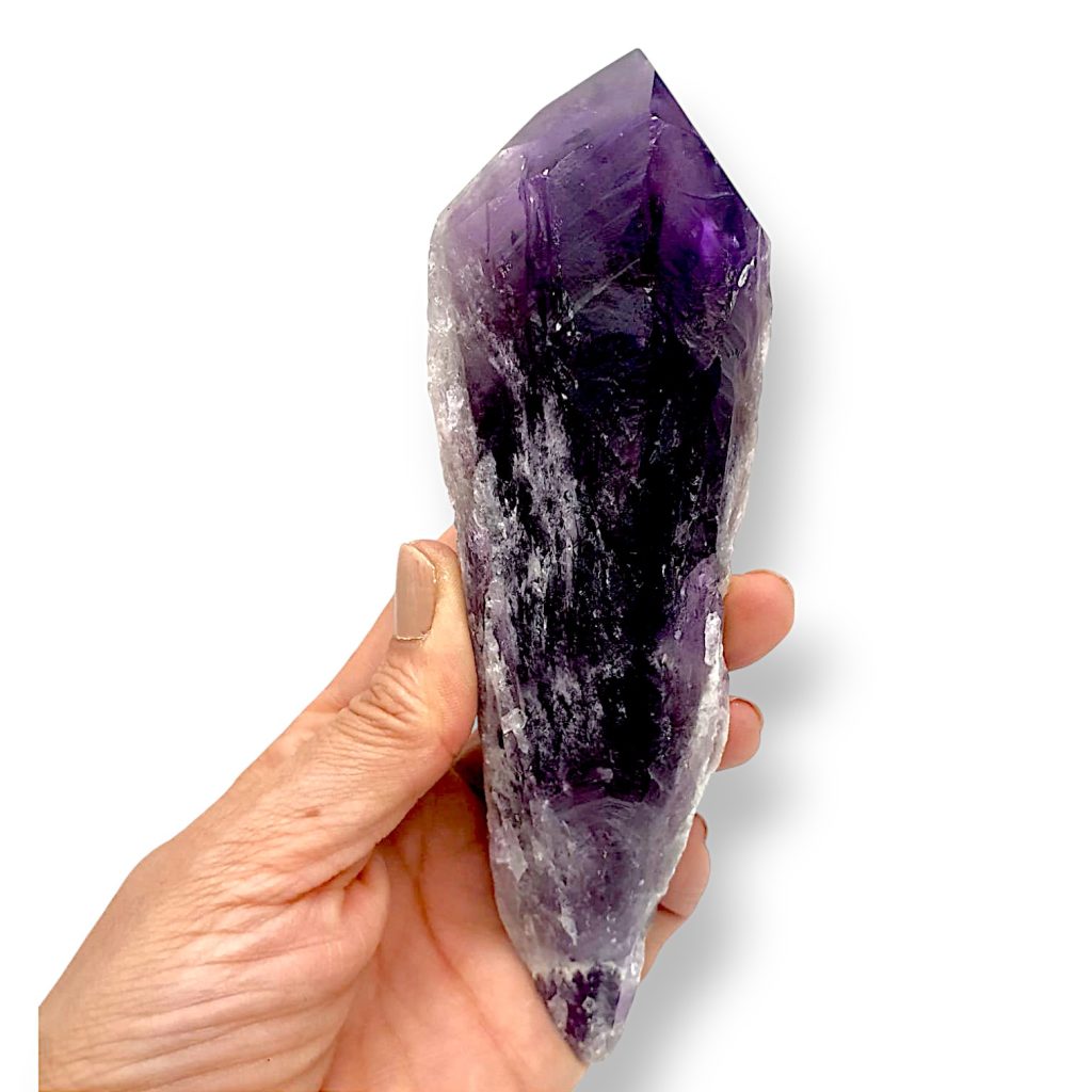 Cetro de amatista sostenido en una mano, con la terminación de violeta muy oscuro y el cuerpo más pálido y lechoso.