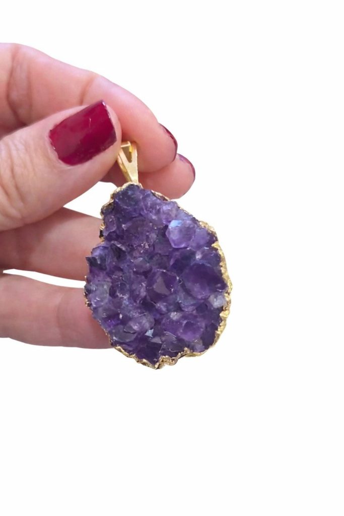 Drusa de amatista entre los dedos: la cara violeta cubierta de puntas pequeñas y el borde dorado siguiendo su contorno