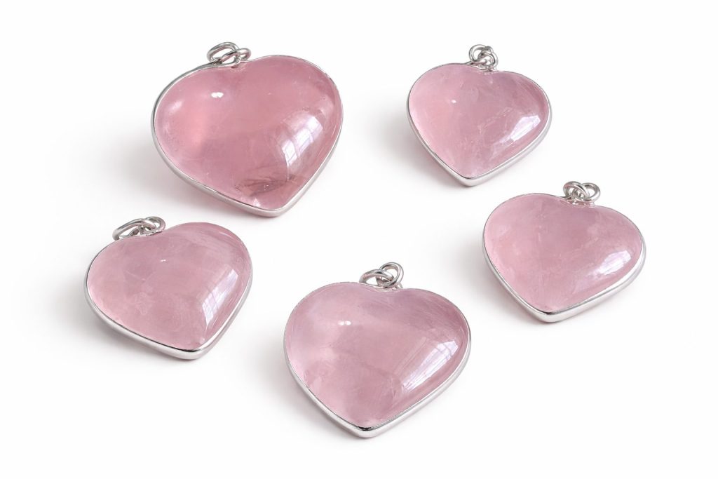 Corazones de cuarzo rosa translúcido con bisel de plata y doble argolla, sobre fondo blanco