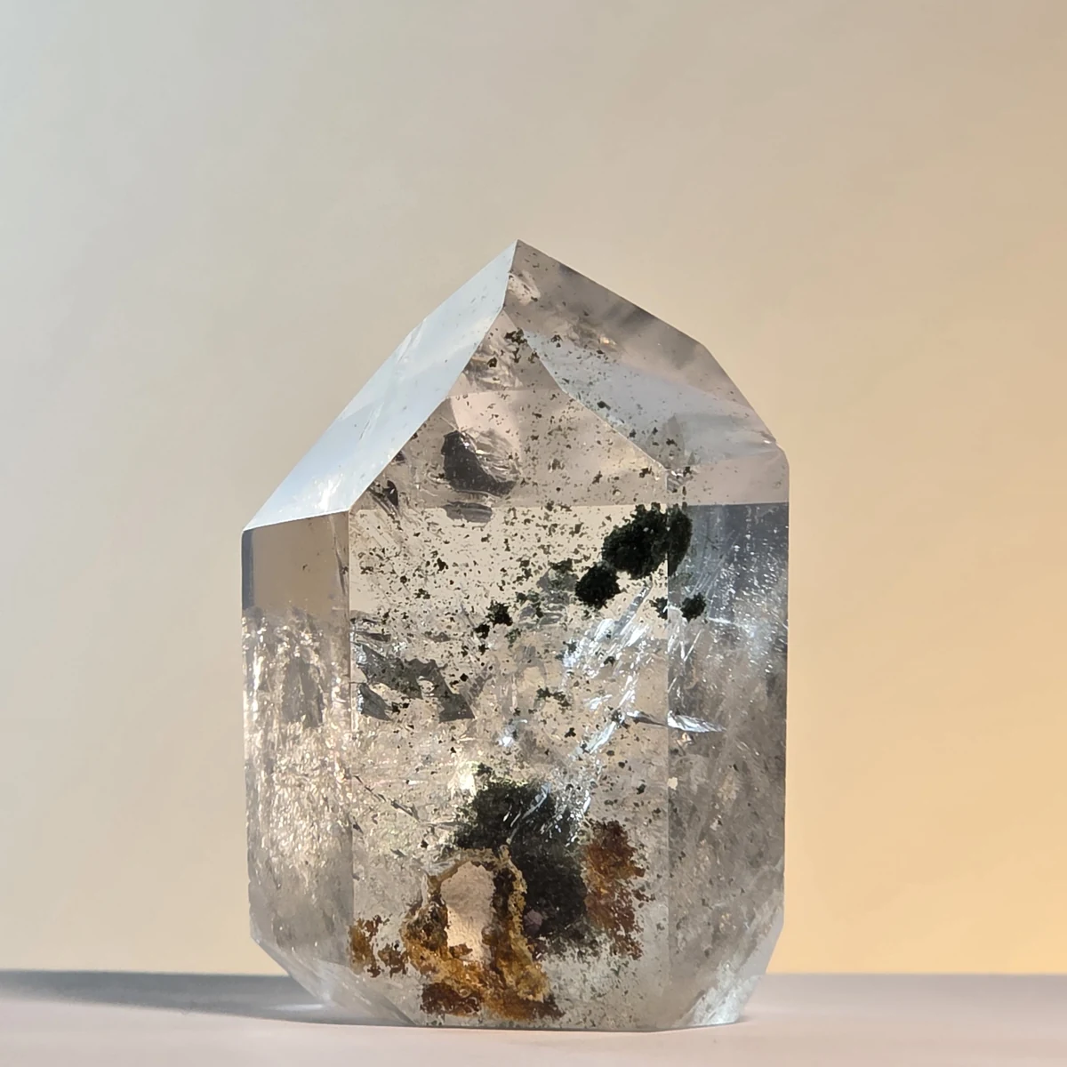 Punta de cuarzo transparente con grumos de clorita casi negros arriba y una masa parda y verde en la base